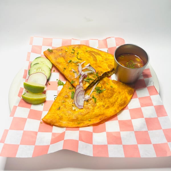 Two golden-brown quesadillas with red onion and cilantro, served with limes, cucumbers, and a side of consommé.