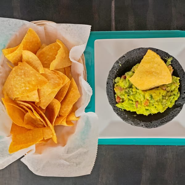 A basket of Mister Taco's tortilla chips next to a molcajete bowl of guacamole with a chip.