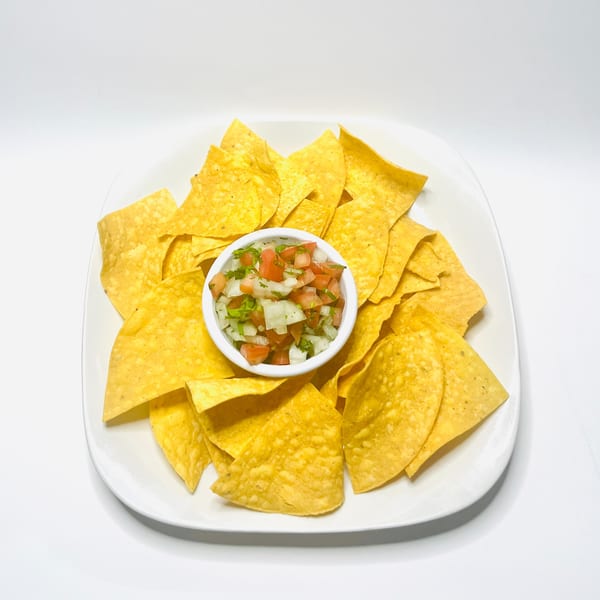 A white plate filled with Mister Taco's golden tortilla chips and a small bowl of fresh pico de gallo.